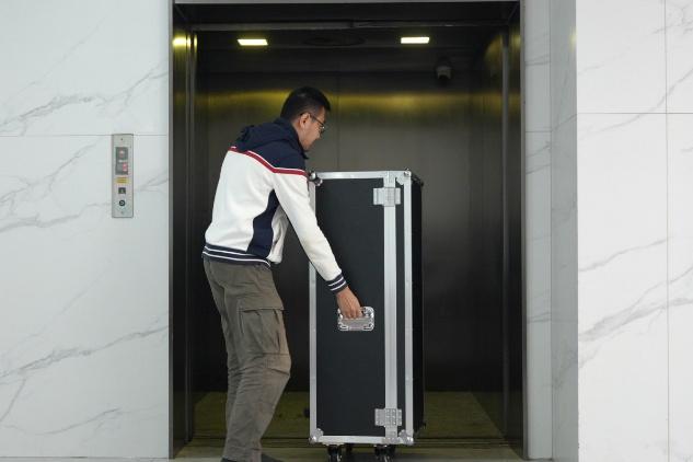 One person wheeling the packed booth case into an elevator